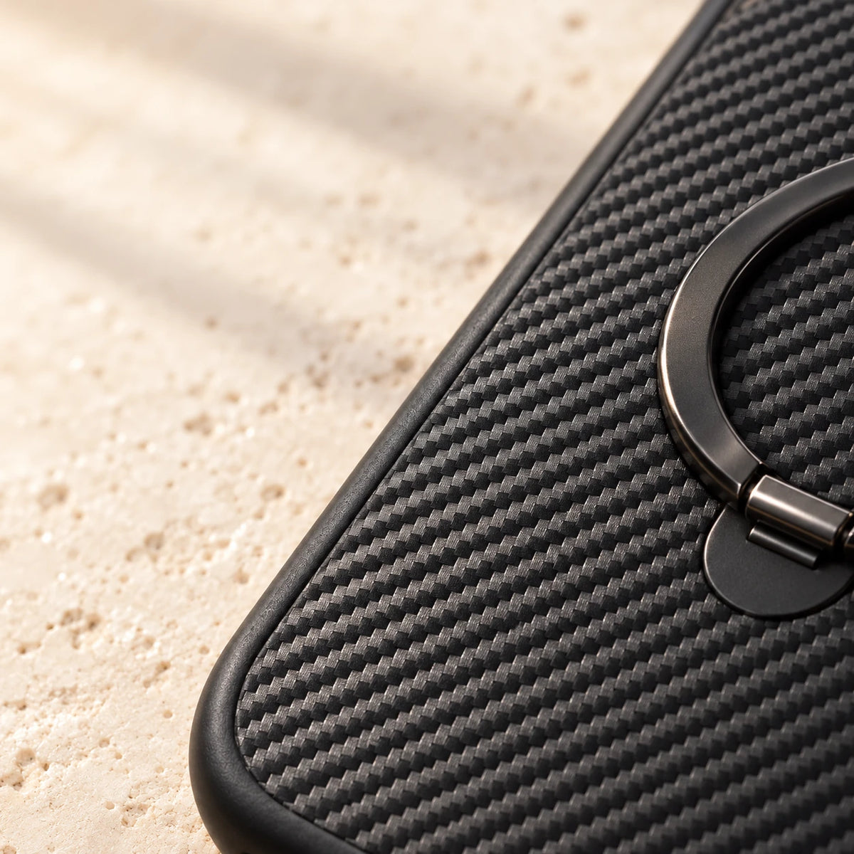 Close-up of diagonal carbon-pattern texture and the folded black ring on a phone case.