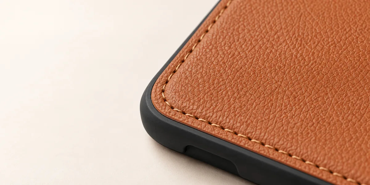 Close-up of grained brown PU leather, stitching and the black edge of a phone case.