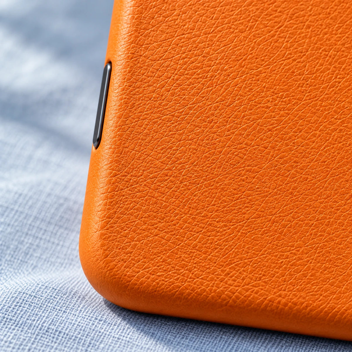 Close-up of fine orange vegan leather grain and the rounded edge of a phone case.